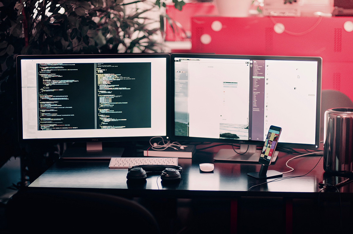 Picture of a programmers desk with two monitors, one of them showing code